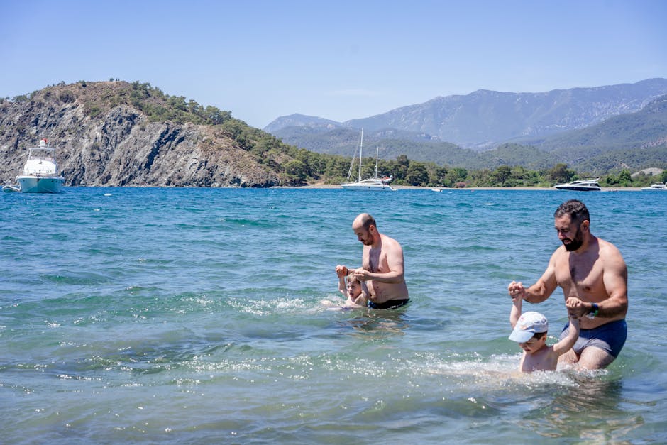 Fathers and sons in swimwear swimming in clean sea water near rocky coast on sunny summer day