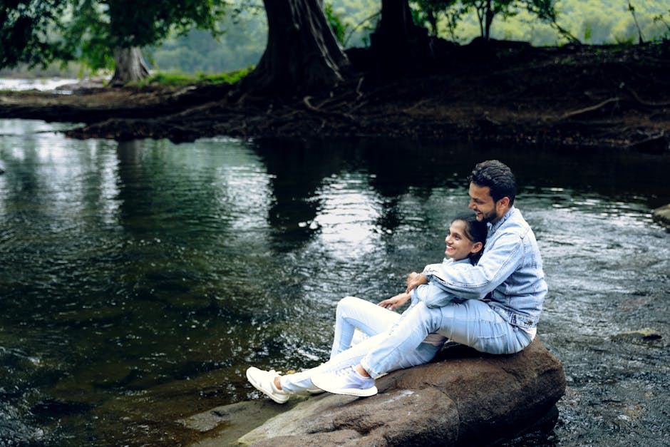 Happy couple sitting by the river, embracing nature's serenity in a rural setting.